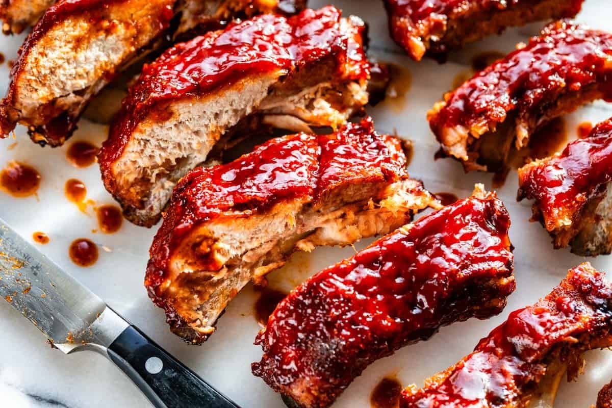 Sliced ribs glazed with bbq sauce on a white background with the knife on the side.