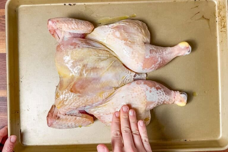 Rubbing the dry brined spatchcock chicken with oil on a cookie sheet.