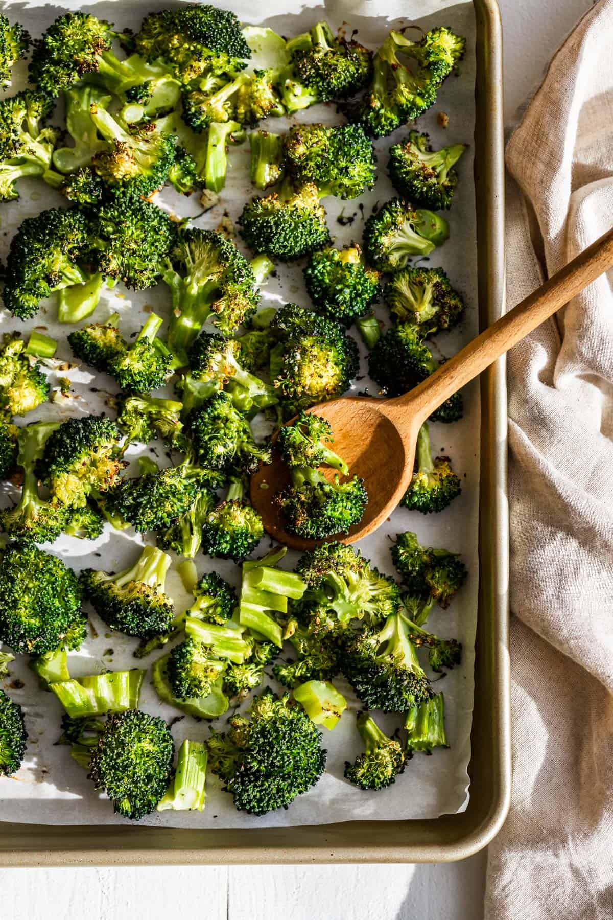 Roasted broccoli floret on a gold cookie sheet with a wood spoon scooping some up.