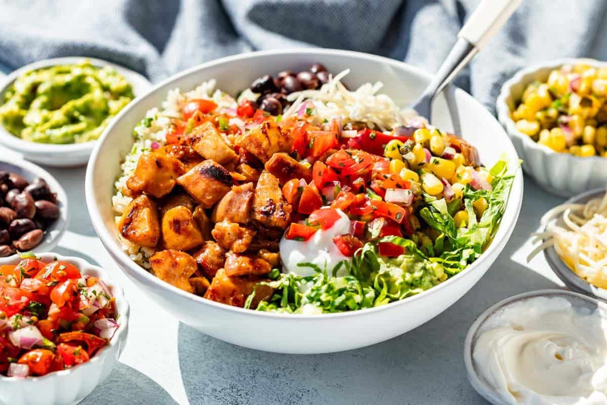 Finished Honey Chicken Burrito Bowls with salsa, cheese, beans, and guacamole around it.