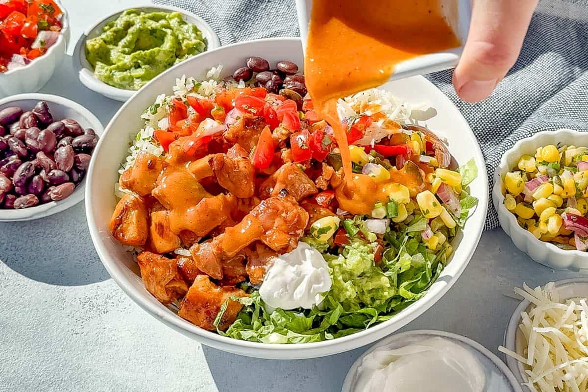 Pouring Chipotle Honey vinaigrette over a chicken burrito bowl.