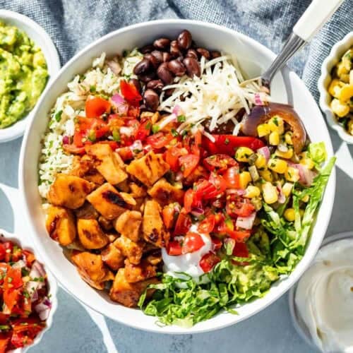 Chopped Chipotle Honey Chicken over a bed of rice, romaine, and black beans with cheese, corn salsa, and Pico de Gallo with bowls of salsa, sour cream, guacamole and more cheese on the side.