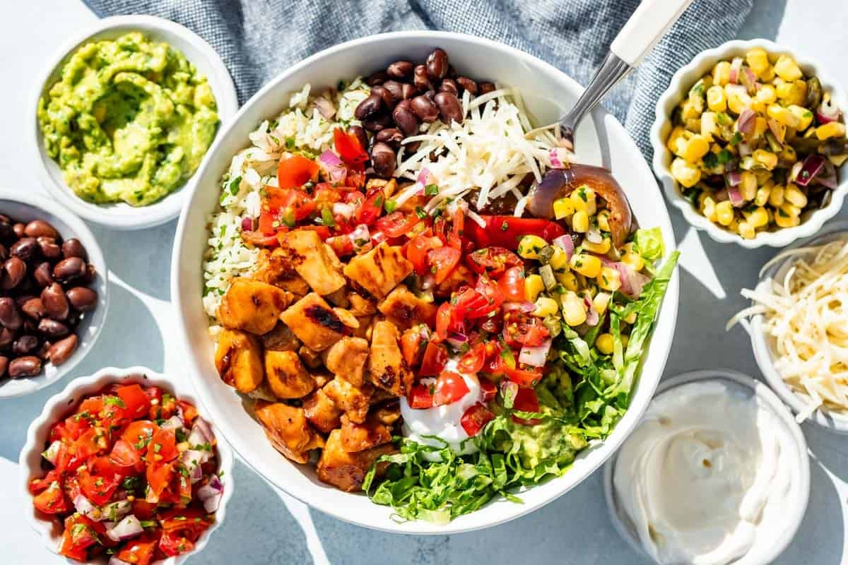 Chopped Chipotle Honey Chicken over a bed of rice, romaine, and black beans with cheese, corn salsa, and Pico de Gallo with bowls of salsa, sour cream, guacamole and more cheese on the side.