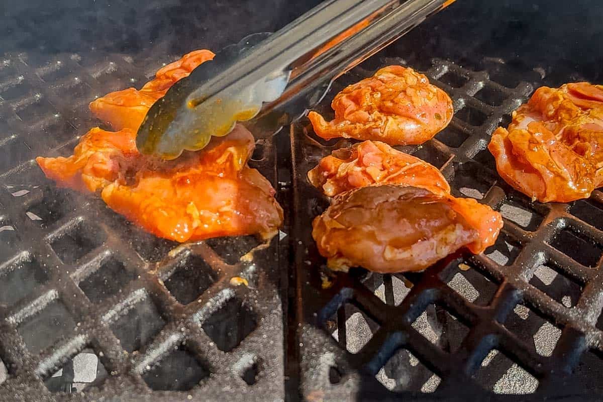 Placing the chipotle honey marinated chicken on a grill with a pair of tongs.