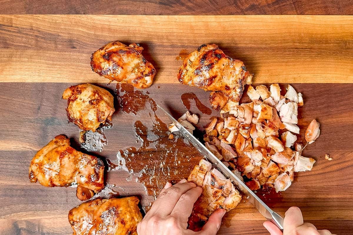 Chopping up the chipotle honey chicken with a large chef's knife on a wood cutting board.