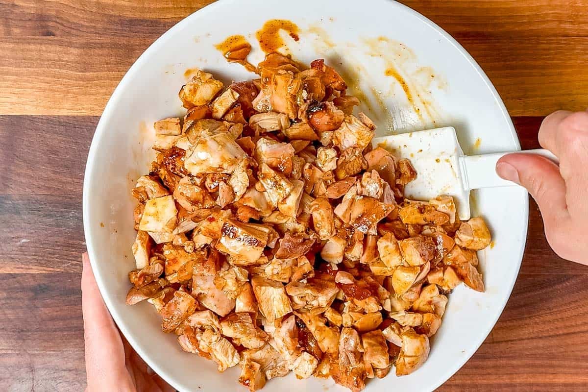 Mixing the chopped chicken with the reserved chipotle honey mixture in a white bowl with a spatula.