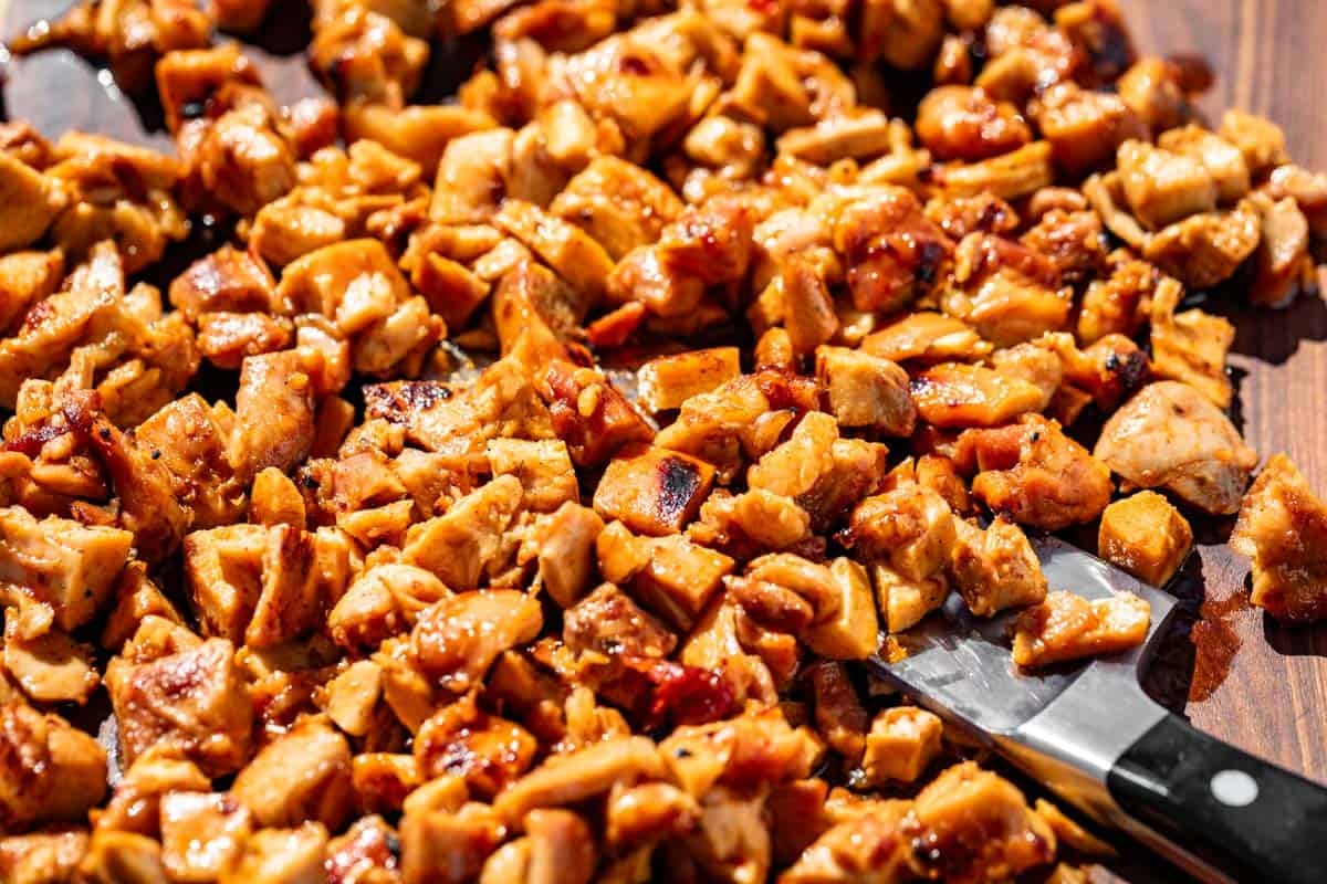 Chopped up Chipotle Honey Chicken on a wood cutting board with a large chef's knife on the side.