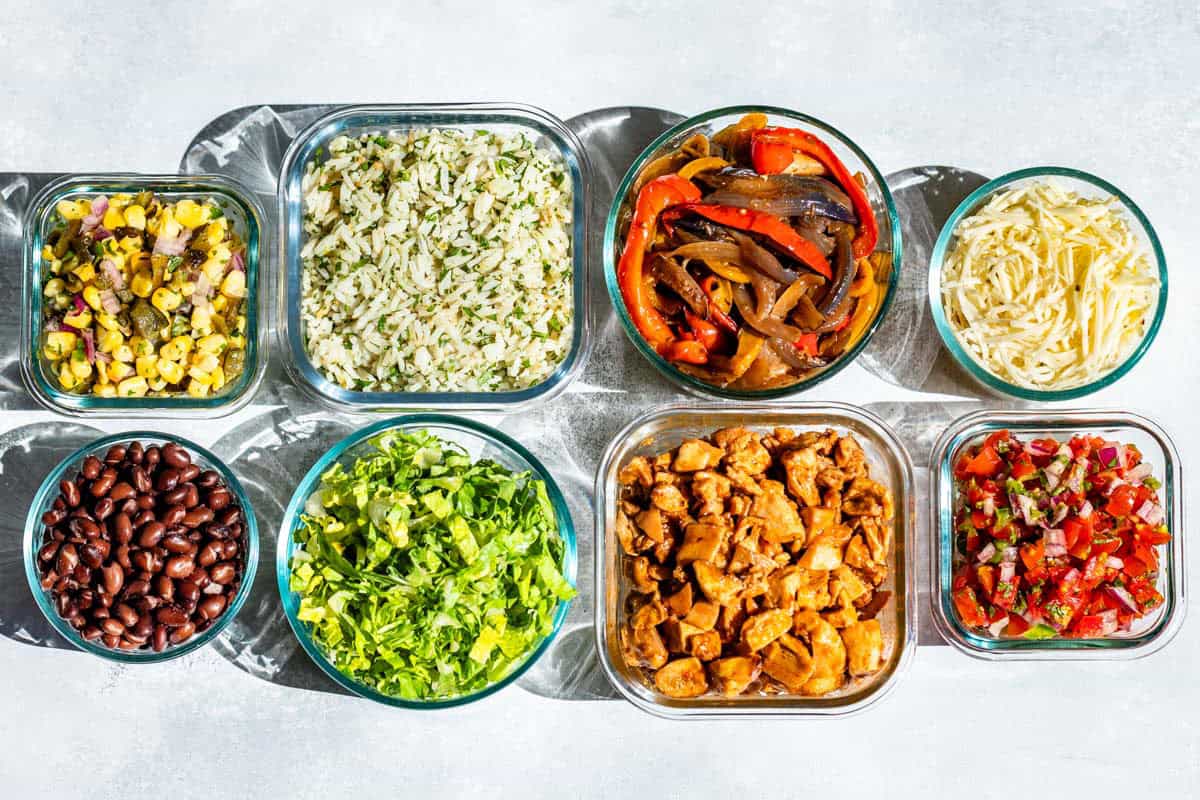 Glass containers of black beans, corn salsa, romaine lettuce, Cilantro Lime Rice, Fajita veggies, chipotle chicken, salsa, and cheese.