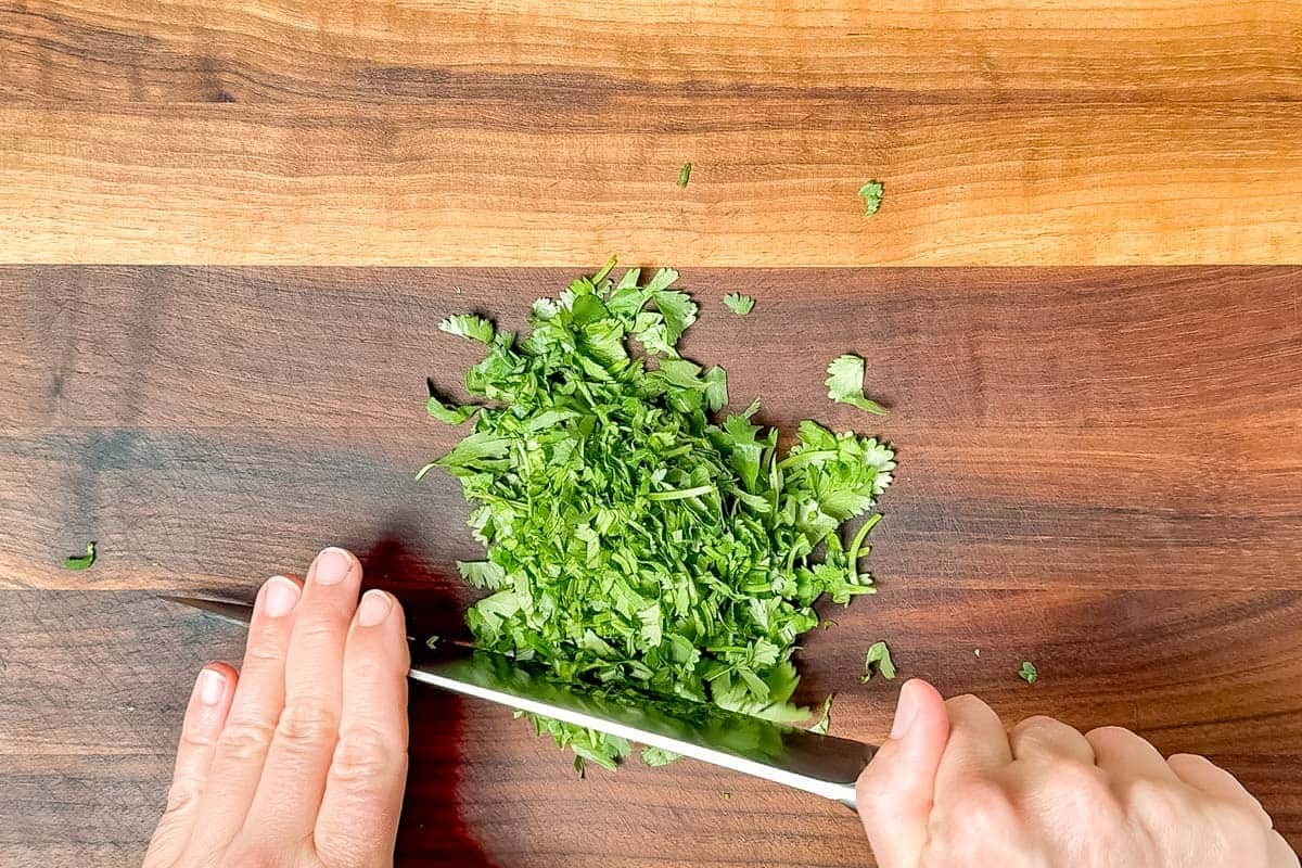Chopping cilantro on a wood cutting board with a chef's knife.