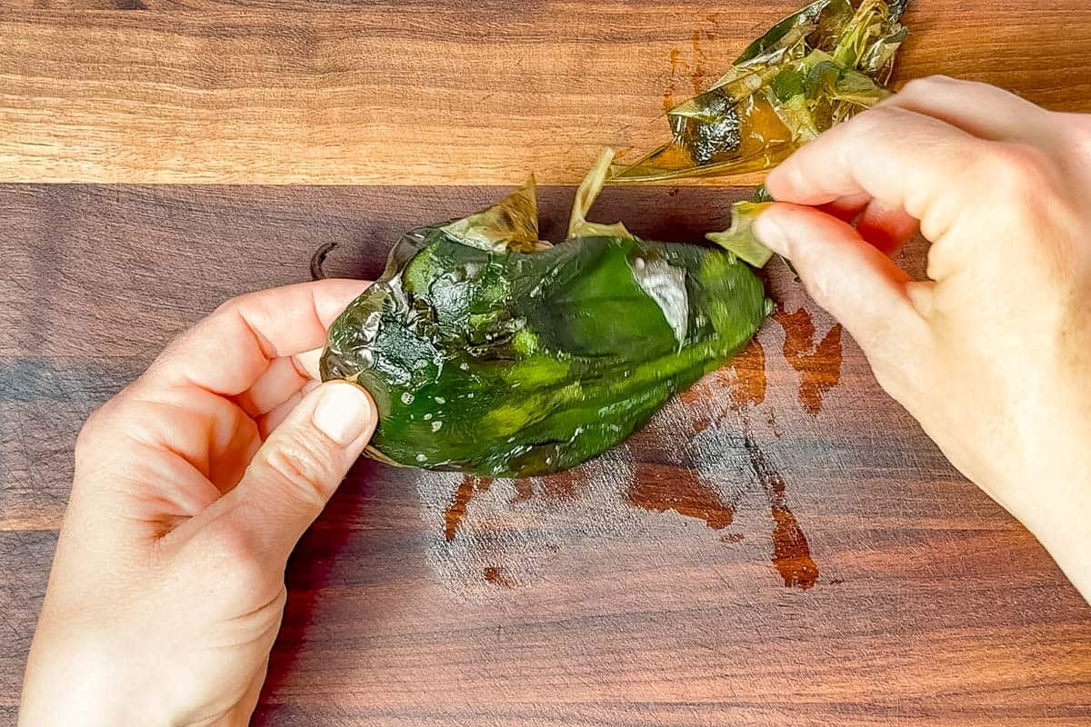 Peeling a roasted poblano on a wood cutting board.