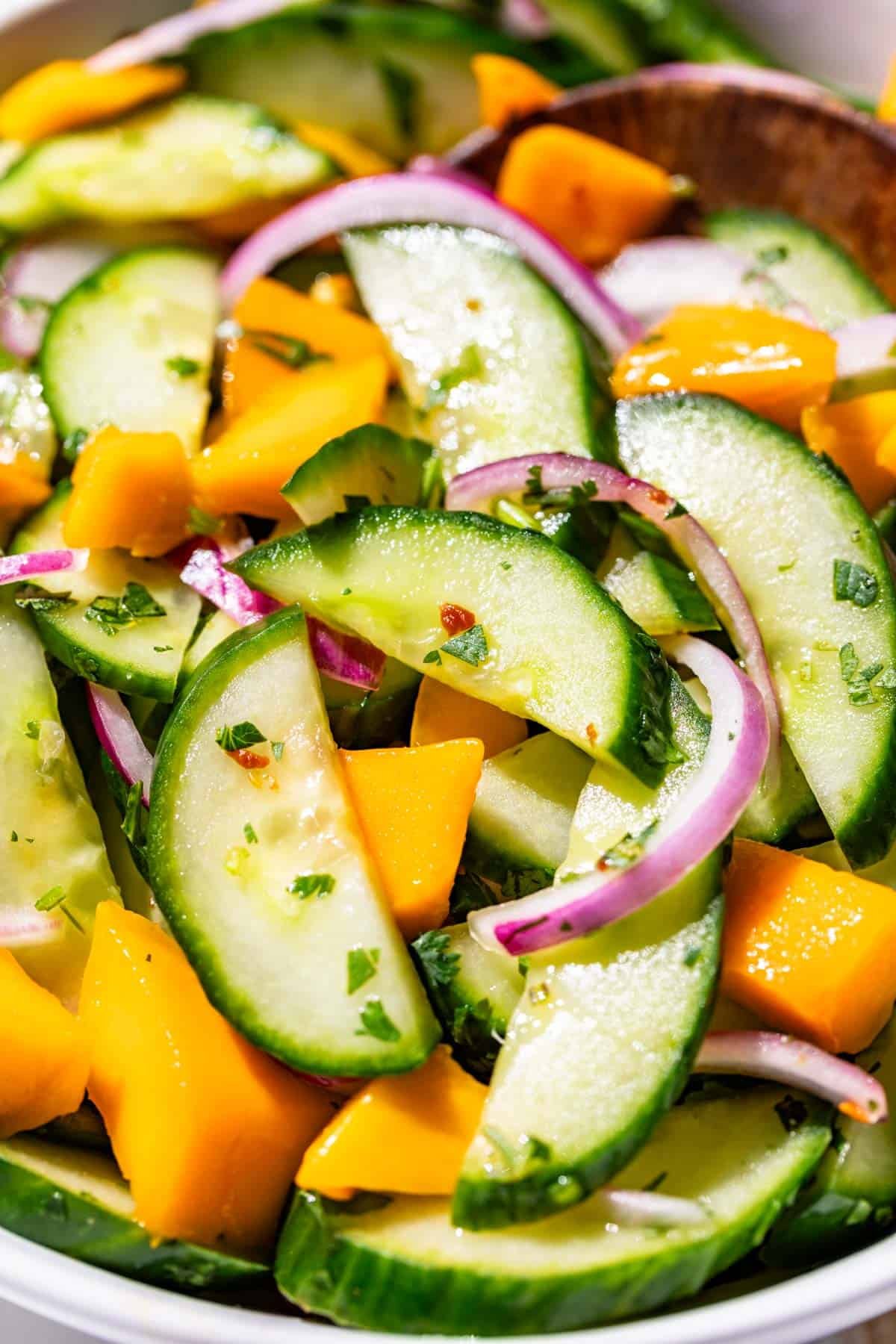 Asian cucumber salad topped with cilantro and mango chunks.