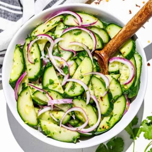 A white bowl filled with Asian cucumber salad with a wood serving spoon and topped with cilantro.