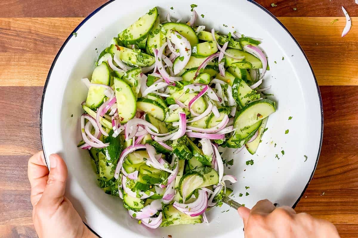 Tossing the Asian cucumber salad in a large white bowl with the dressing.