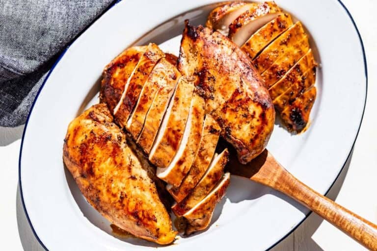 Four cooked chicken breasts on a blue rimmed white oval platter with a wood serving spatula.