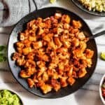 A black bowl of chopped Chipotle Chicken surrounded by bowls of Pico de Gallo, corn, guacamole, and rice with lime wedges.