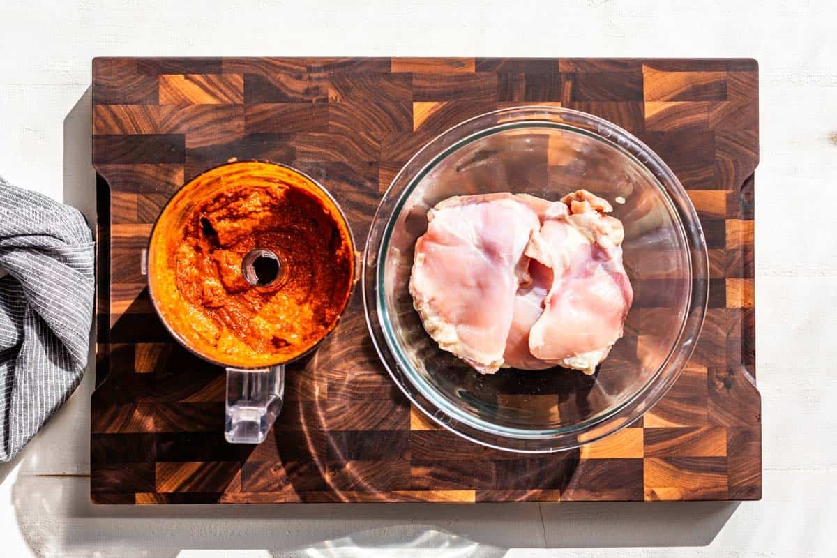 The adobo marinade in a food processor next to a glass bowl with chicken thighs in it.