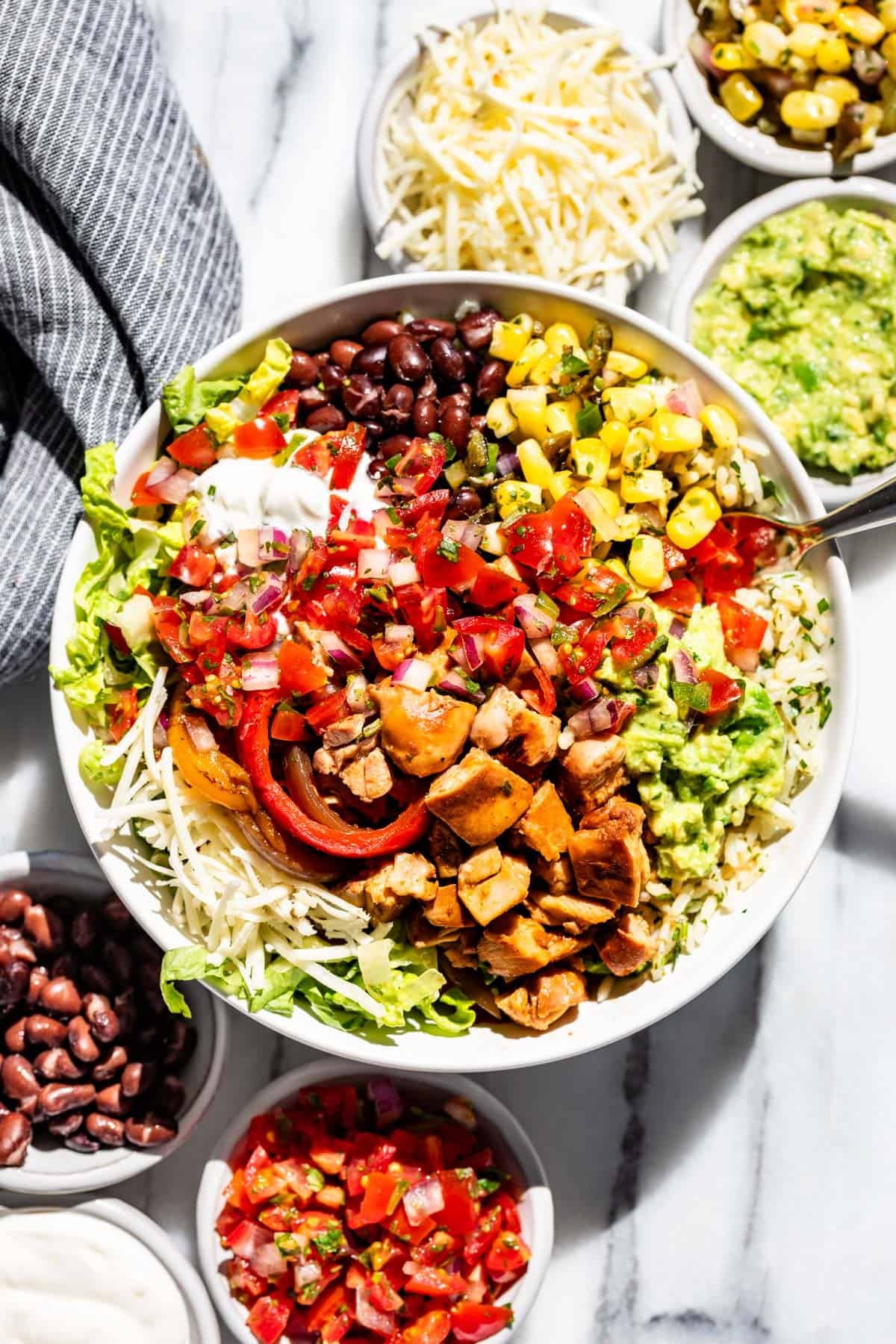 Chipotle chicken burrito bowls surrounded by small bowls of black beans, sour cream, pico de gallo, cheese, corn salsa, and guacamole.