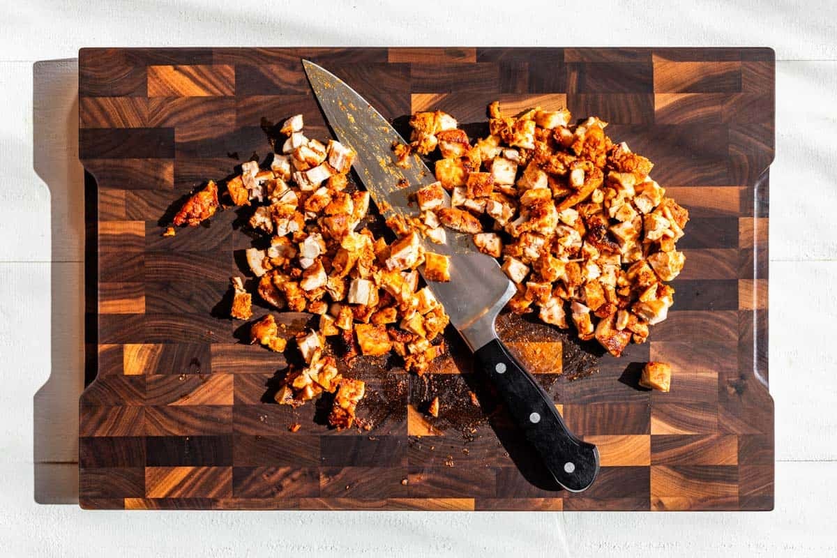 The chipotle chicken being chopped up on a wooden cutting board.