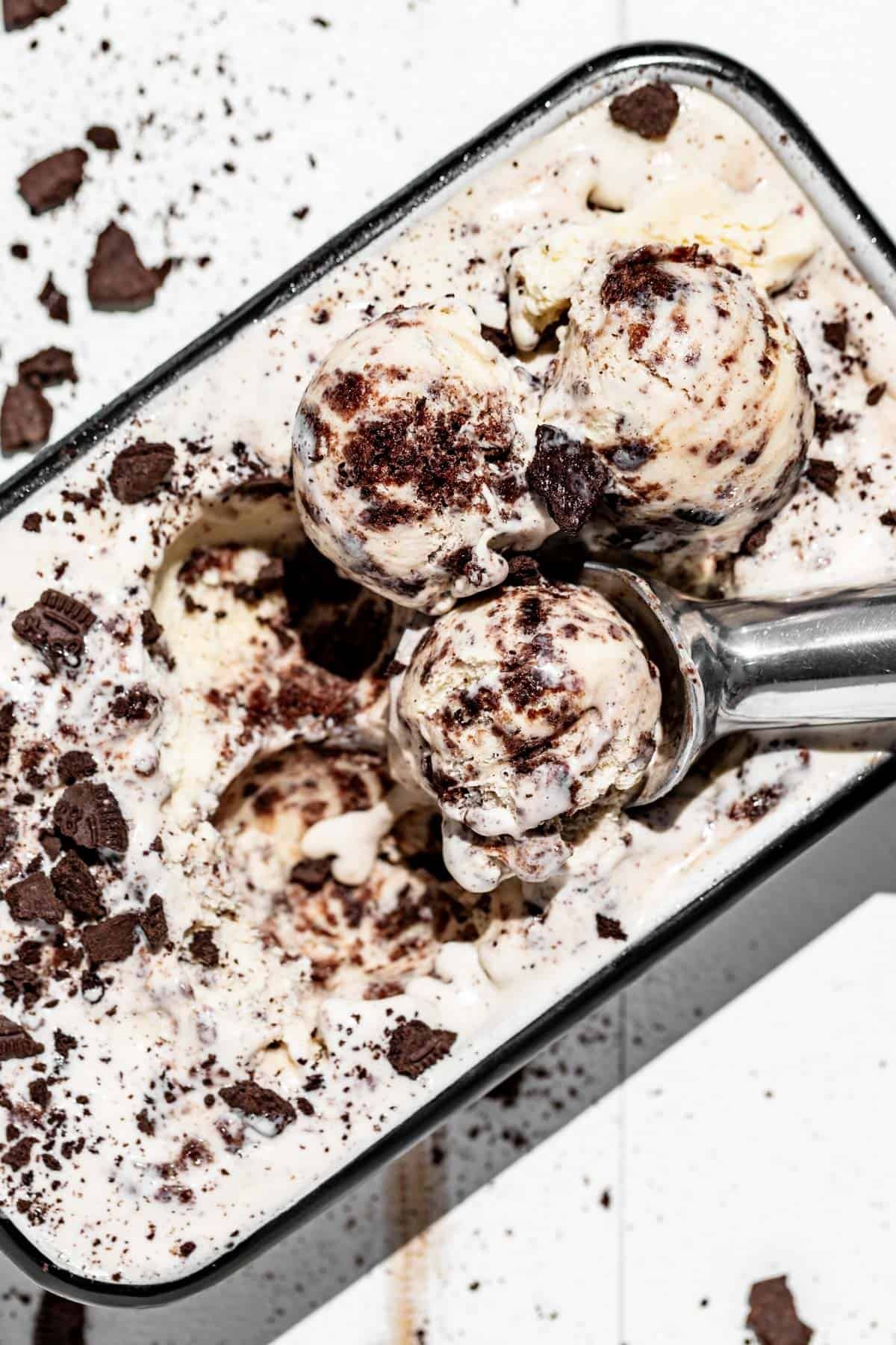 Three scoops of cookies and cream ice cream sitting on top of a container of ice cream.