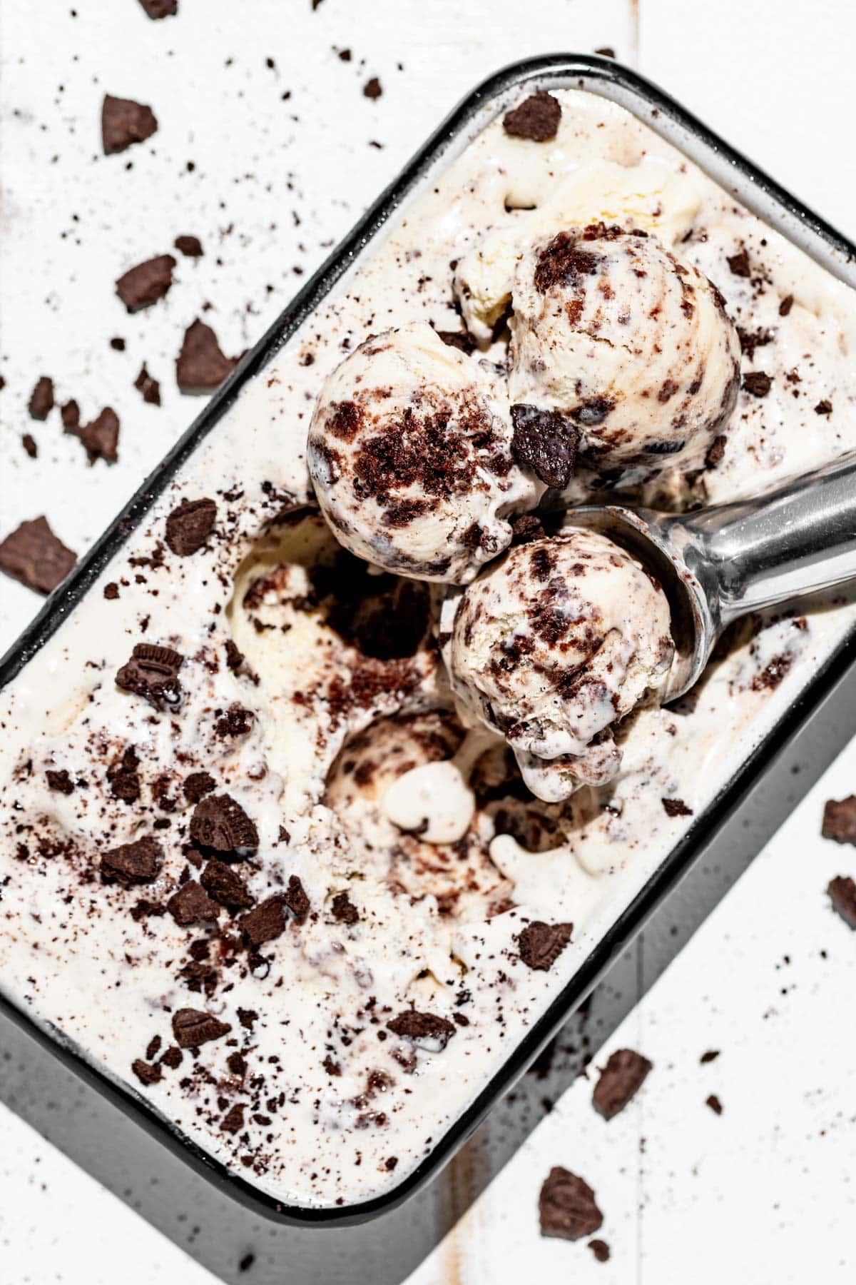 A black rimmed white square dish filled with cookies and cream ice cream with a cookie scoop scooping up ice cream.
