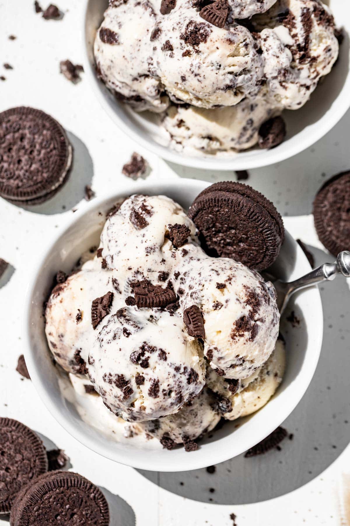 Two white bowls filled with scoops of Cookies and Cream Ice Cream with crushed oreos on top and oreo cookies around the bowls.