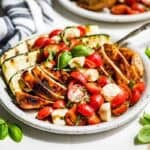 Balsamic Grilled Chicken topped with Caprese Salad on a pottery plate with basil sprigs around it.