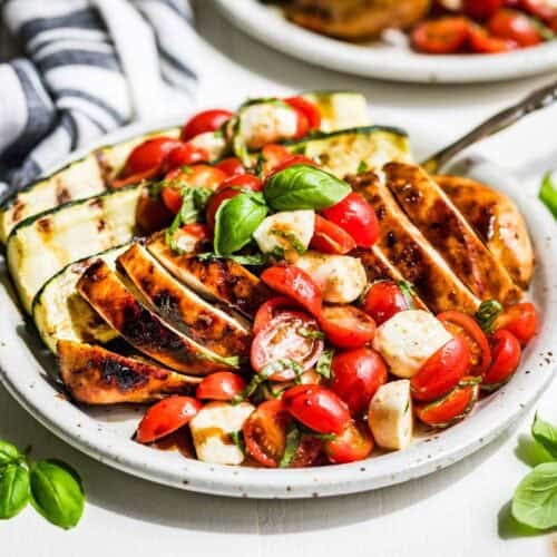 Balsamic Grilled Chicken topped with Caprese Salad on a pottery plate with basil sprigs around it.