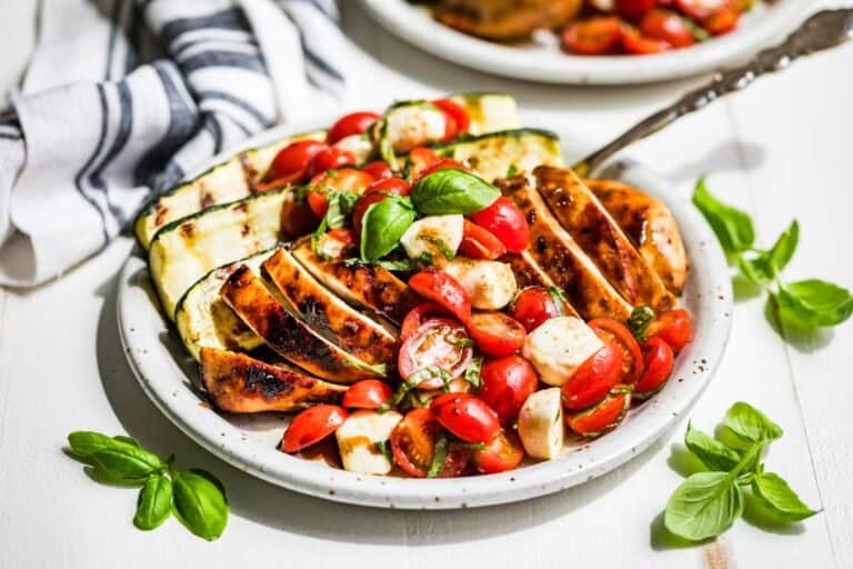 Balsamic Grilled Chicken topped with Caprese Salad on a pottery plate with basil sprigs around it.