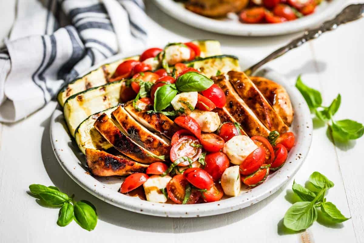 Balsamic Grilled Chicken topped with Caprese Salad on a pottery plate with basil sprigs around it.