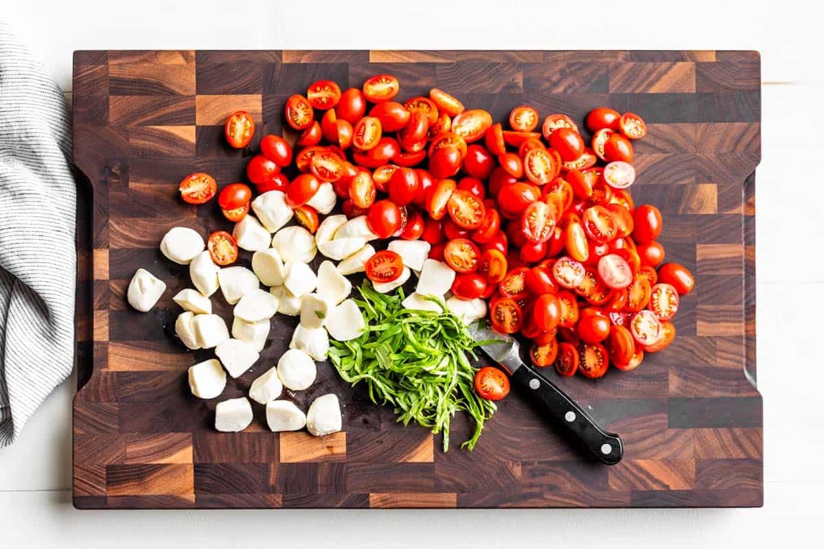 Cut up tomatoes and mozzarella with sliced basil on a wooden cutting board.