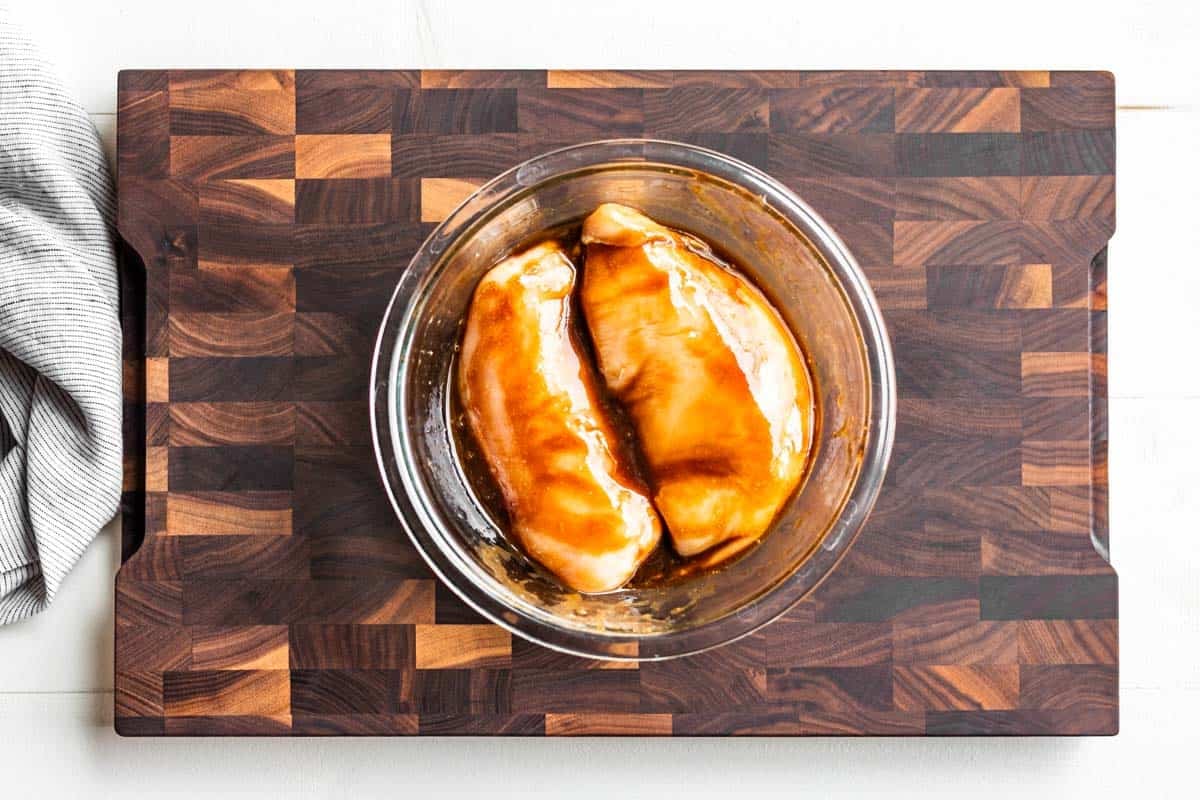 Marinating Balsamic Chicken in a glass bowl on a wooden cutting board.