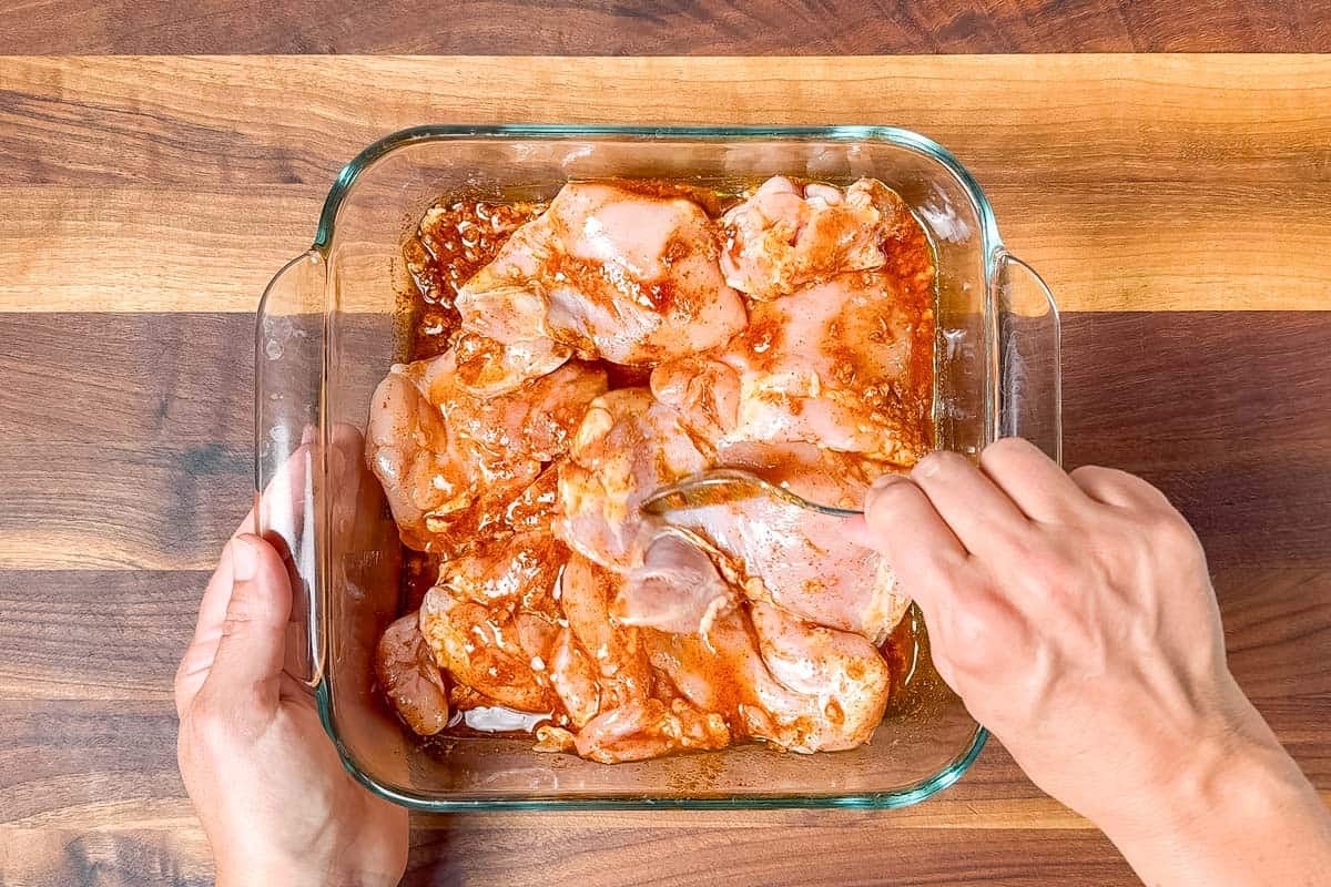 Turning the chicken thighs in the marinade with a metal spoon.