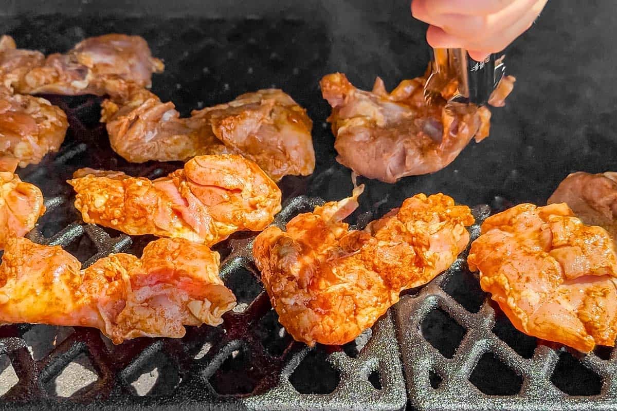 Placing the marinated chicken on a hot grill with metal tongs.