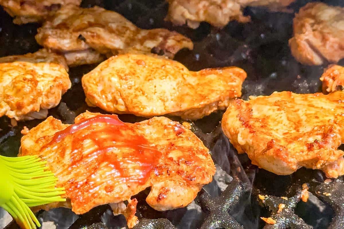 Brushing the turned chicken thighs with bbq sauce with a green silicone brush.