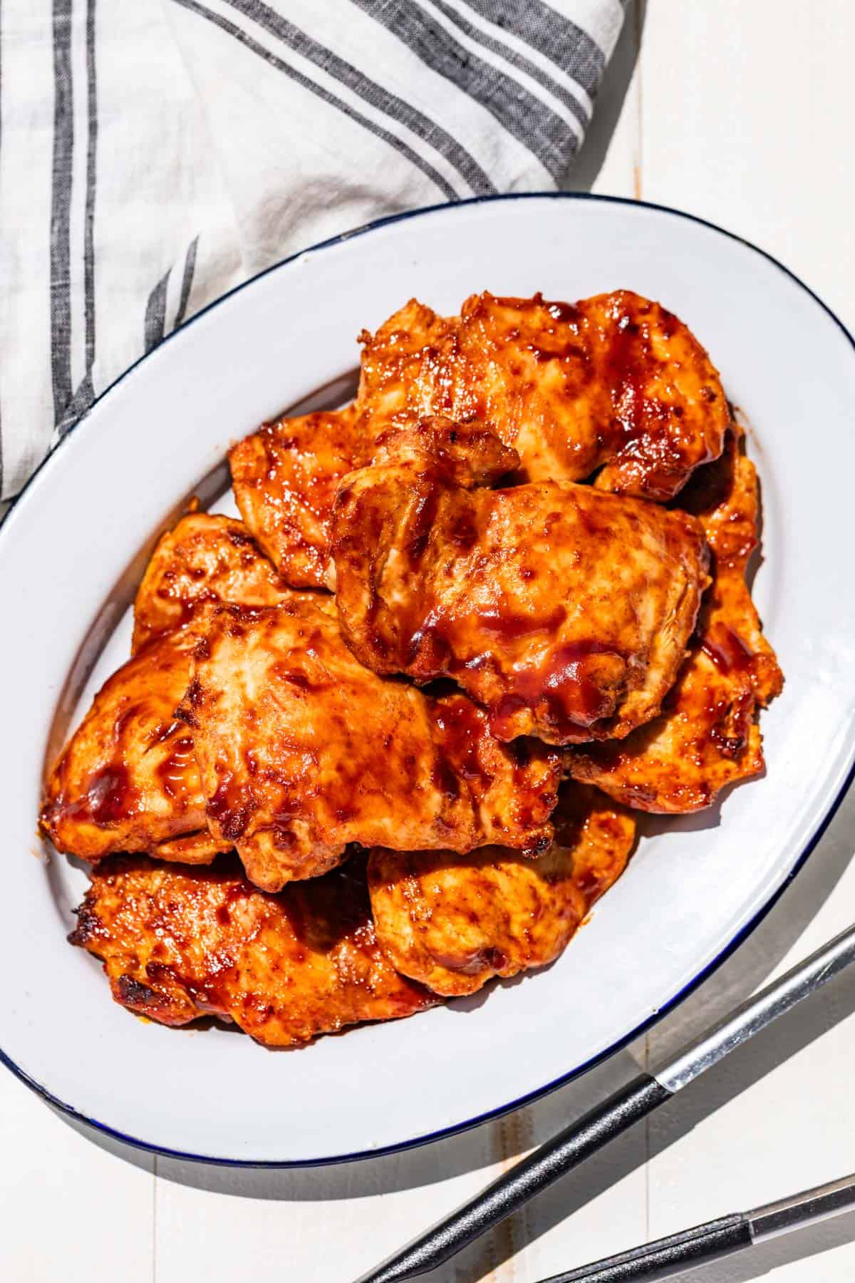Grilled Chicken Thighs on a blue rimmed white platter with metal tongs on the side.