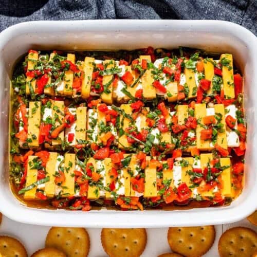 Marinated cheddar cheese and cream cheese in a small baking dish surrounded by crackers.