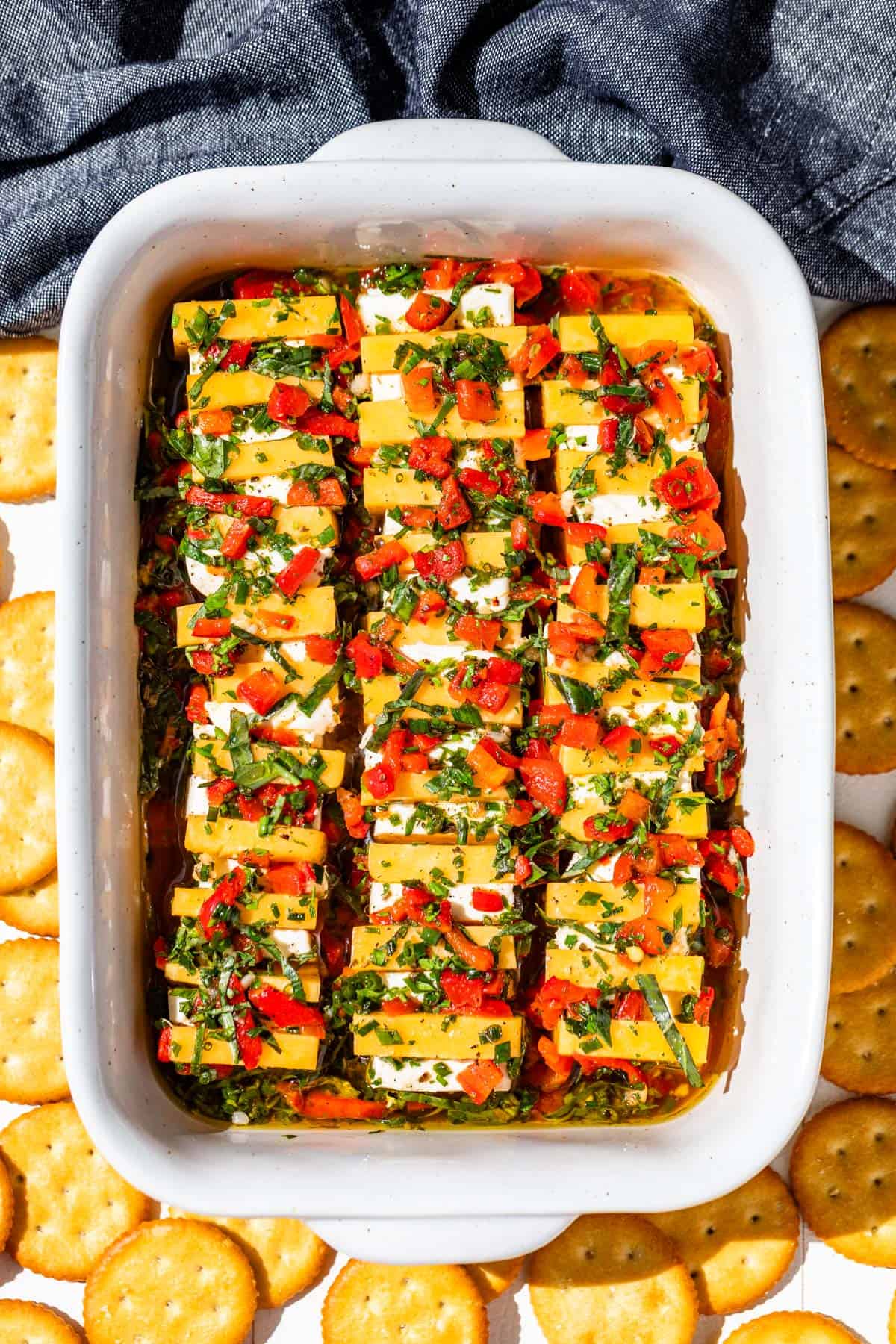 Cubes of cheddar cheese alternated with cream cheese topped with a red bell pepper herb dressing in a baking dish.