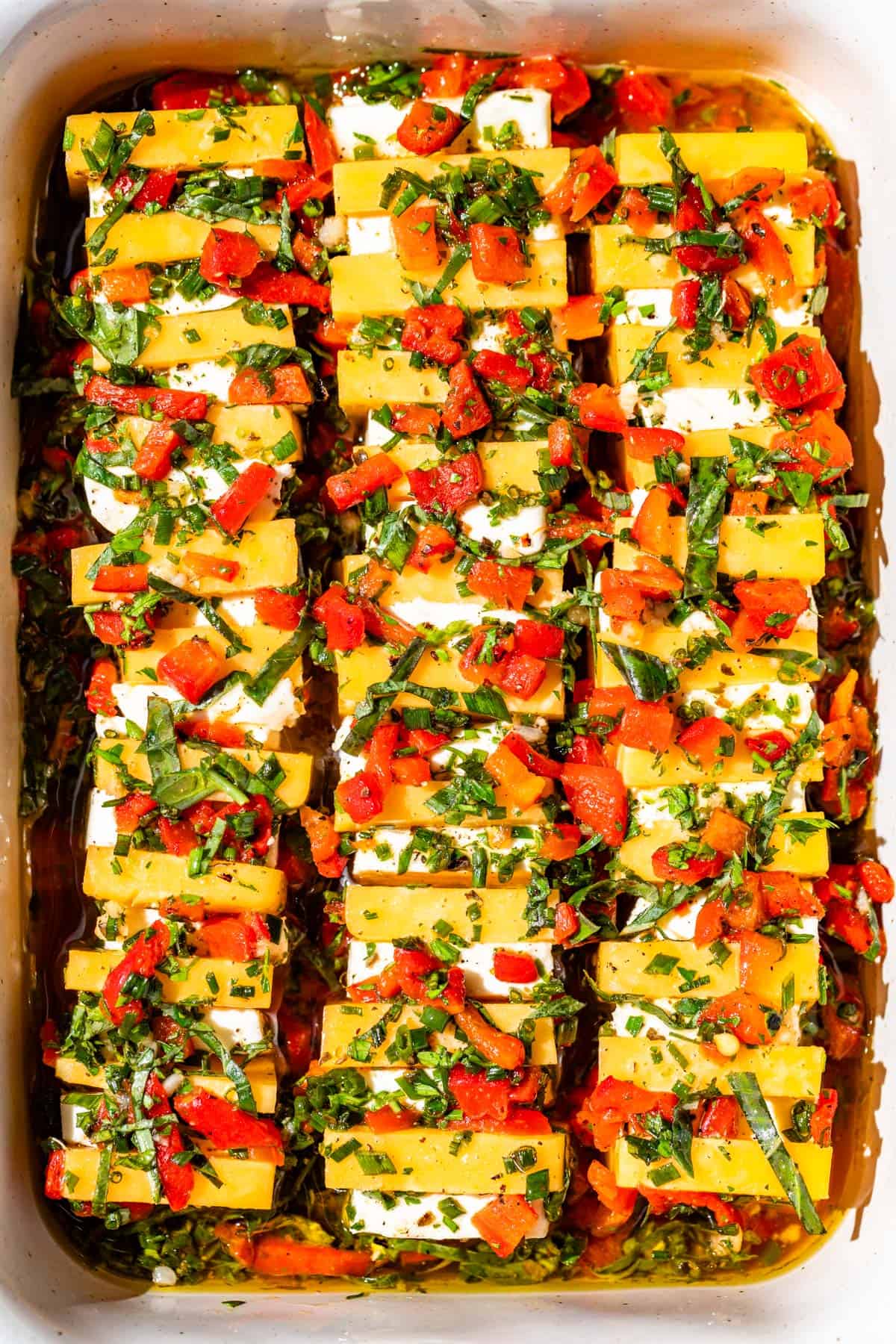 Cheddar cheese and cream cheese in rows of alternating cubes topped with a red bell pepper herb marinade.