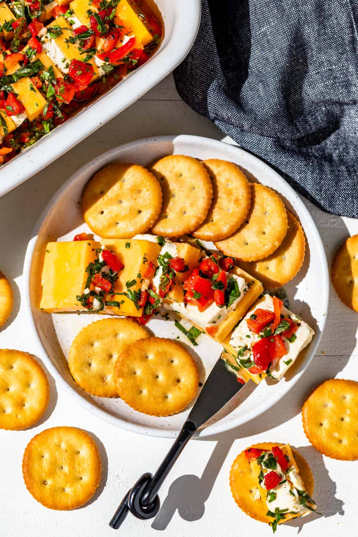 A small white plate with crackers and marinated cheese with a serving knife.