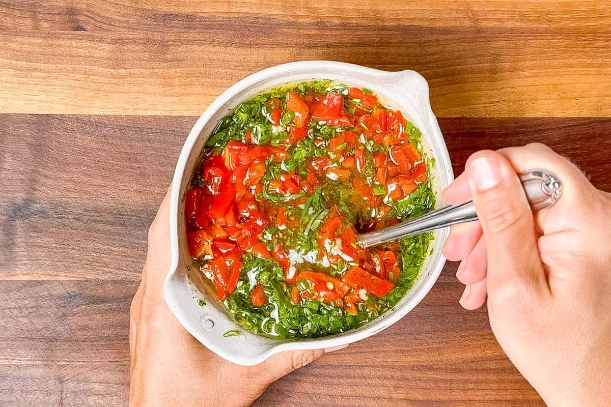 Mixing the red bell pepper herb marinade mixture in a pottery bowl.