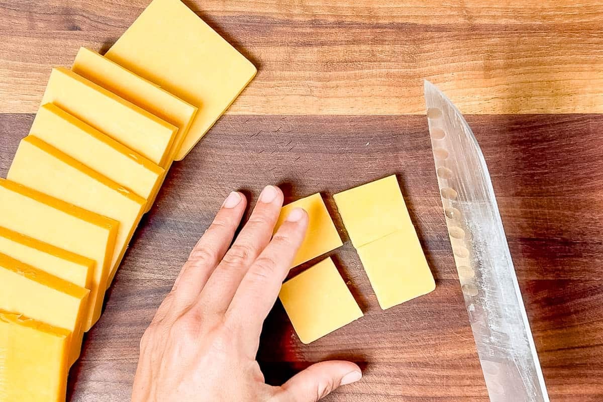 Cutting cheddar cheese into small squares with a chef's knife.