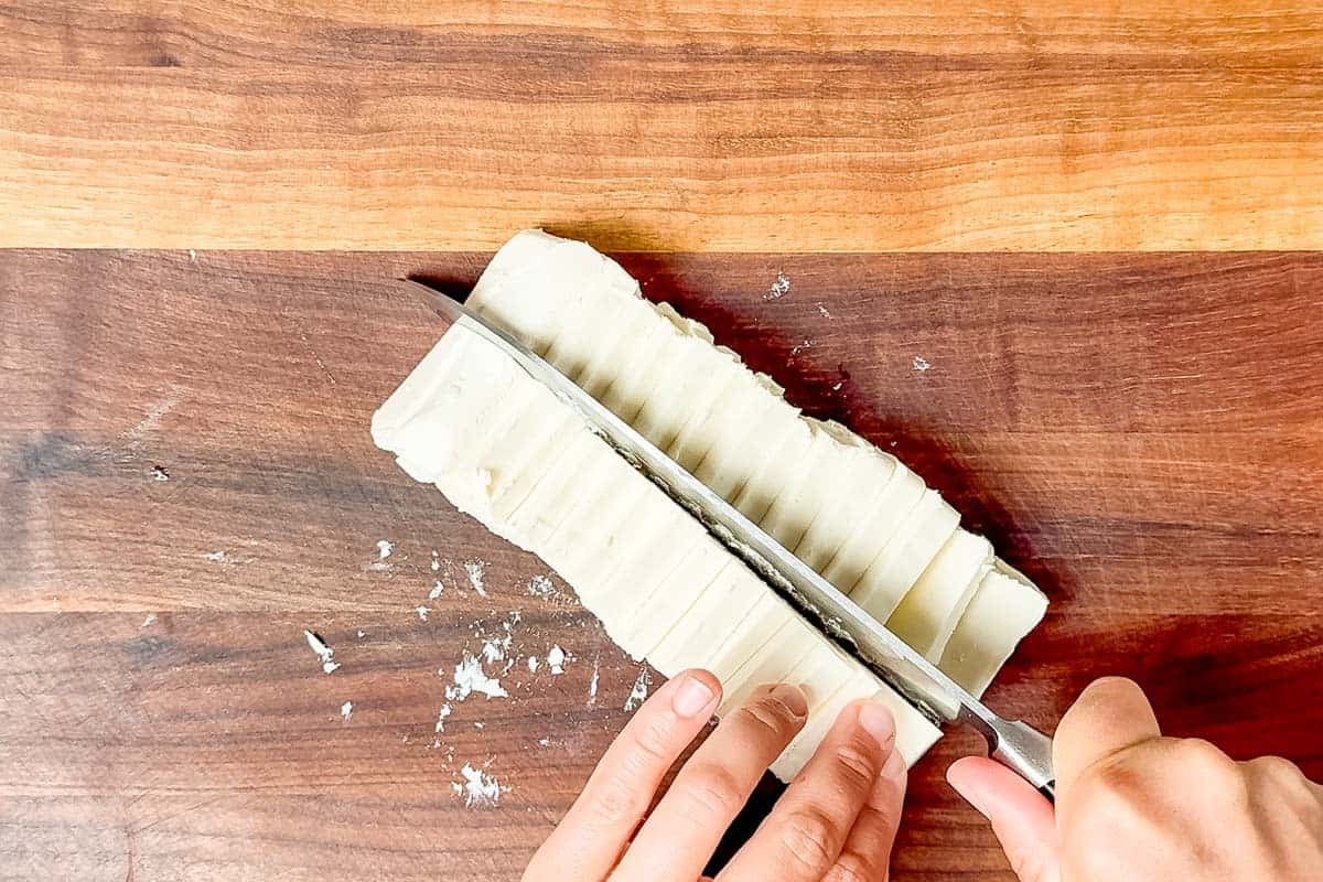 Cutting cream cheese into squares with a chef's knife.