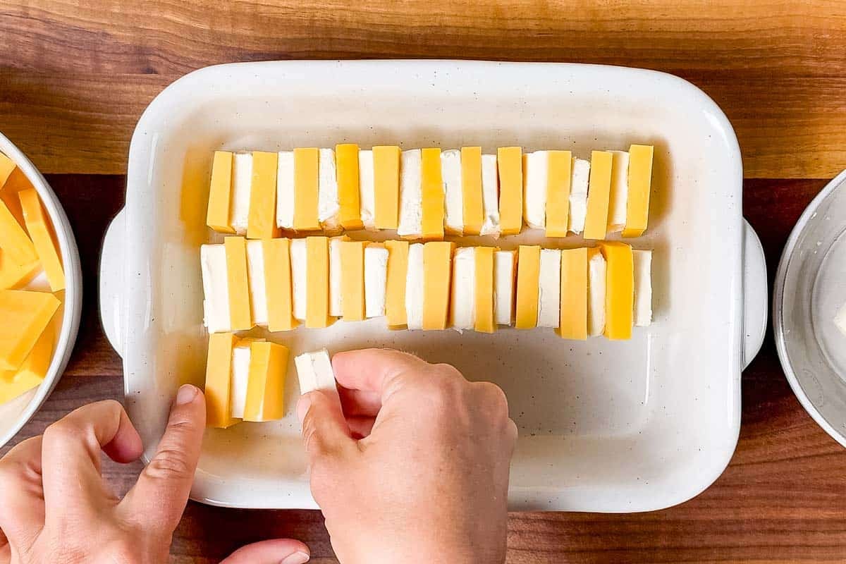 Making rows of alternating cheddar cheese and cream cheese in a small baking dish.
