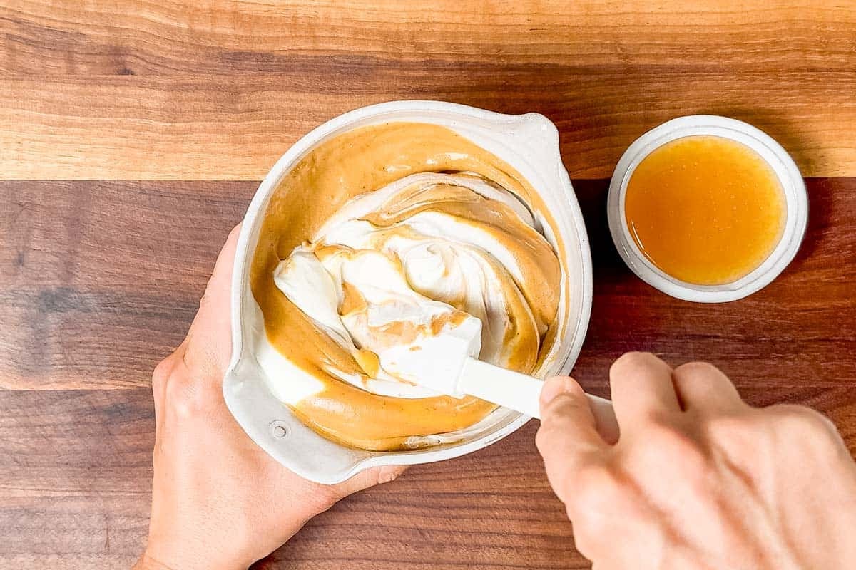 Mixing Greek yogurt with peanut butter in a pottery bowl with a spatula.