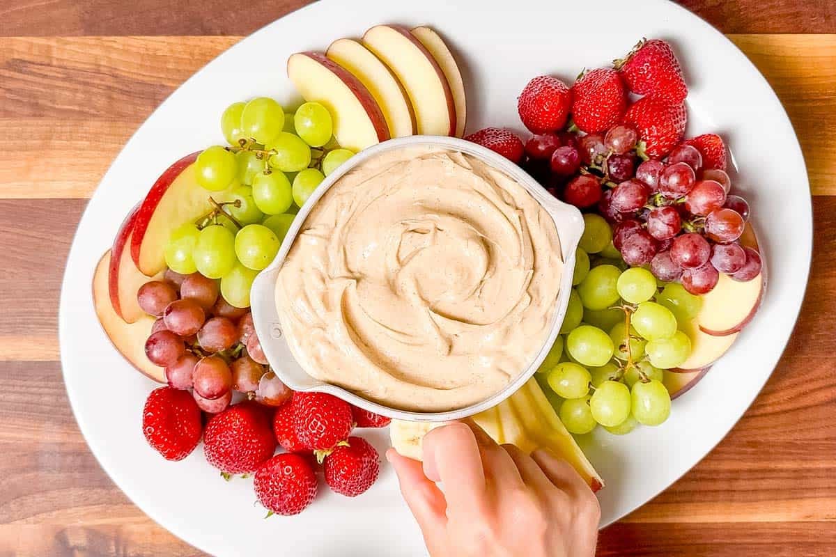 Placing grapes, apples, strawberries, and banana slices around the dip.