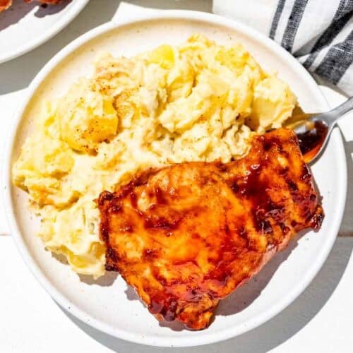 Grilled bbq chicken thighs and potato salad on two white plates.