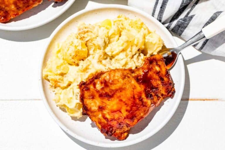Grilled bbq chicken thighs and potato salad on two white plates.
