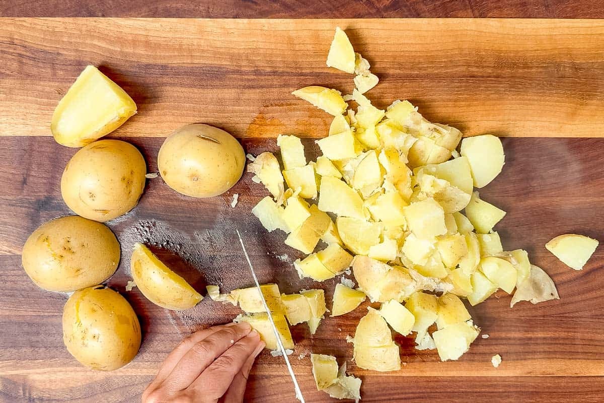 Cutting up the cooked potatoes with a knife on a wood cutting board.
