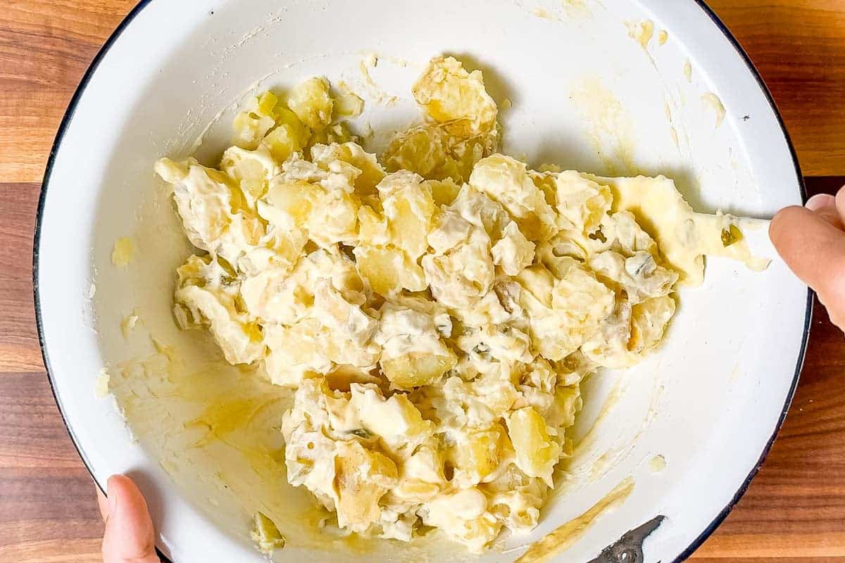 Mixing the cooked potatoes with mayonnaise and Dijon mustard with pickles in a large white bowl.