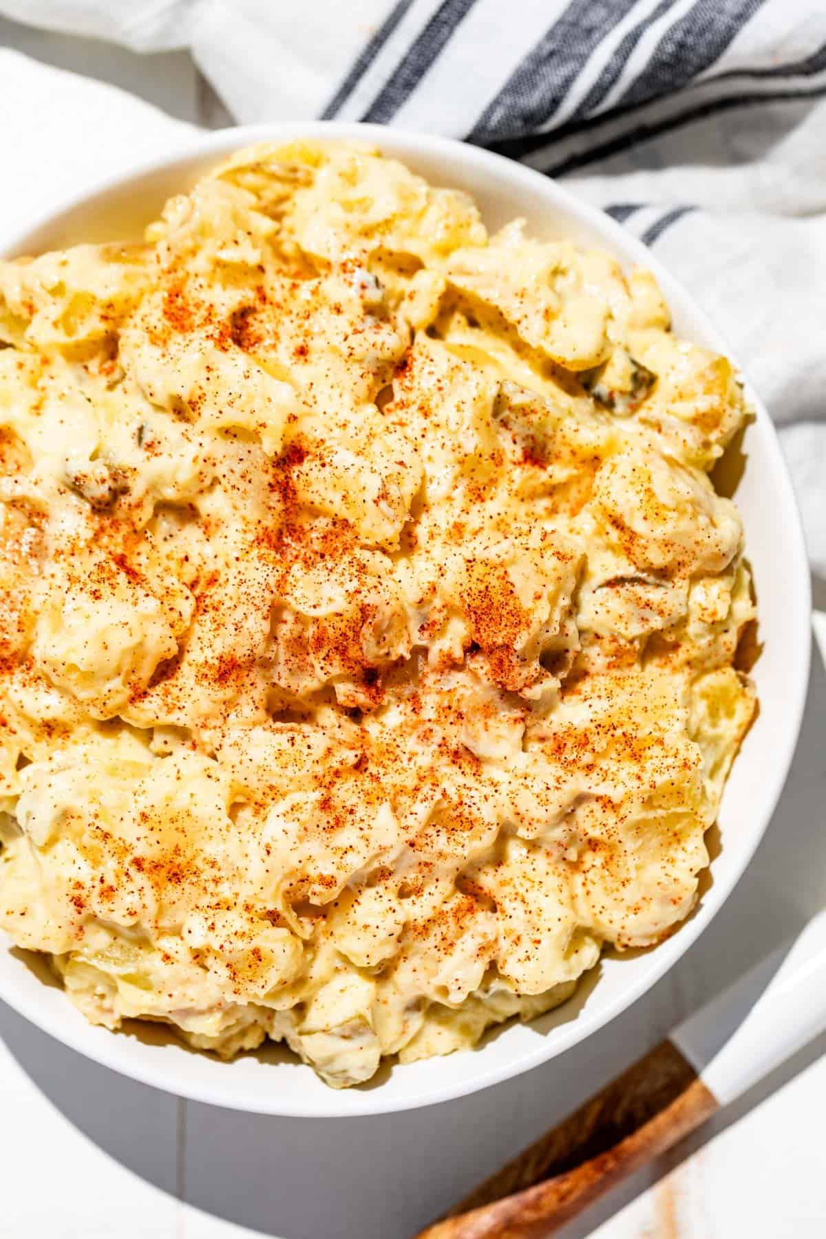 Potato salad in a white bowl sprinkled with smoked paprika with a wood handled spoon on the side.